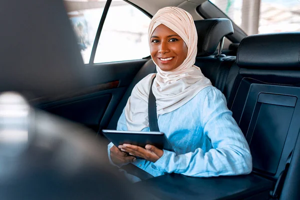 車の中で座っている間 タブレットを使用してヒジャーブの若いイスラム教徒の女性 車の中で働くイスラム教徒のビジネス女性 — ストック写真