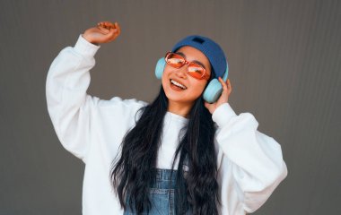 Şapkalı şık Asyalı genç kadın sokakta kulaklıkla müzik dinliyor..