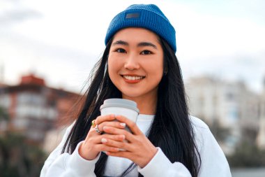 Açık havada dururken kahve ya da çay içen Asyalı genç bir kadının portresini yakından çek..