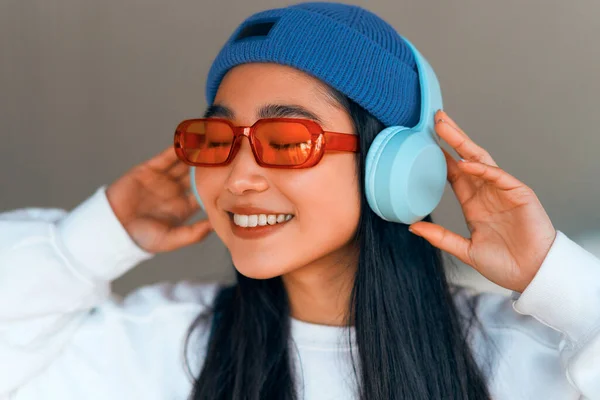 ストリートでヘッドフォンで音楽を聴く帽子のスタイリッシュなアジアの若い女性 — ストック写真