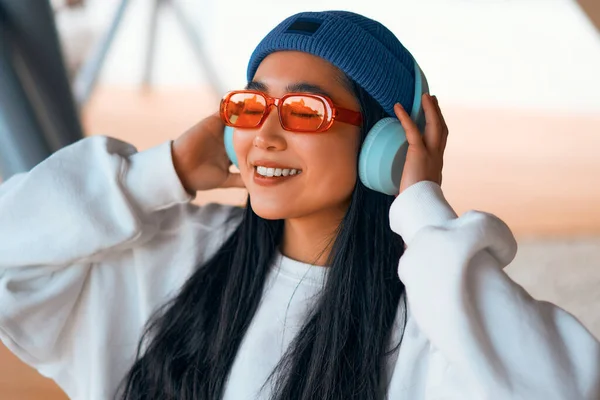 ストリートでヘッドフォンで音楽を聴く帽子のスタイリッシュなアジアの若い女性 — ストック写真