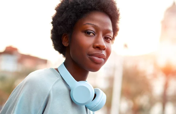 African American woman listening to music in headphones with afro hairstyle on the street and spending a fun weekend.