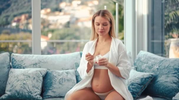 迷人的孕妇正坐在靠窗的蓝色天鹅绒沙发上 吃着酸奶 健康食品概念 怀孕的最后几个月 — 图库视频影像
