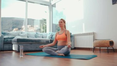 Spor kıyafetli hamile bir kadın evin oturma odasındaki lastik bir paspasın üzerinde otururken egzersiz ya da yoga yapıyor. Hamilelik sırasındaki spor.