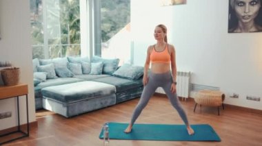 Spor giyimli hamile bir kadın evin oturma odasındaki lastik bir paspasın üzerinde egzersiz yapıyor. Hamilelik boyunca spor ve yoga.