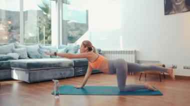 Spor giyimli hamile bir kadın evin oturma odasındaki lastik bir paspasın üzerinde egzersiz yapıyor. Hamilelik boyunca spor ve yoga.