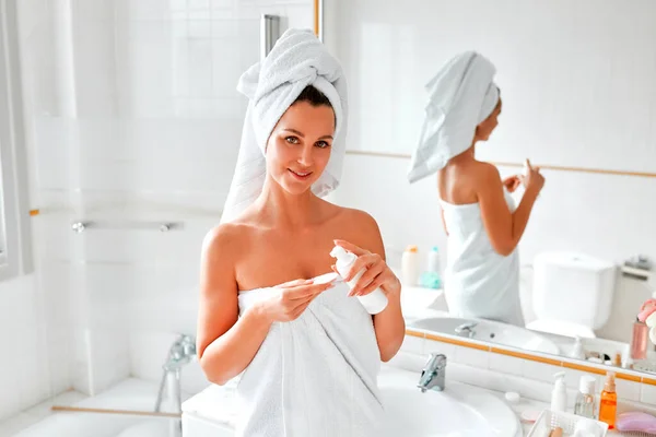 鏡の前の浴室に立つタオルのブロンドの女性は 洗顔フォームとシリコンブラシを使用して顔と体のスキンケアのための彼女の朝のルーチンを行います 美容とスパの手順 — ストック写真