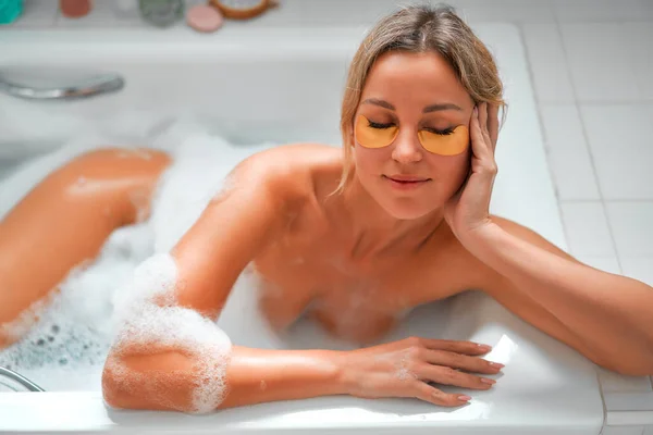 漂亮的女人躺在一个白色的泡沫浴池里 享受和放松 用眼罩补丁 早上例行公事化妆品和温泉疗程 — 图库照片