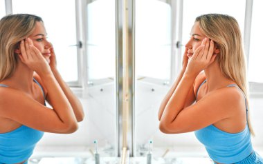 Mavi iç çamaşırlı sarışın bir kadın aynanın karşısında banyoda duruyor ve yüz ve vücut bakımı için sabah rutinini yapıyor. Kozmetoloji ve kaplıca prosedürleri.