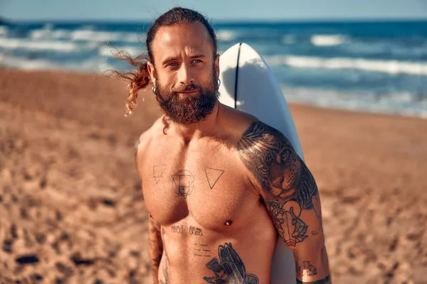 Biały Surfer Brodaty Tatuażami Długimi Włosami Kąpielówkach Deską Surfingową Pobliżu — Zdjęcie stockowe