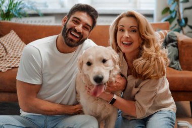 Genç bir çift evdeki oturma odasının penceresinde oturmuş labrador köpeklerine sarılıp oynaşıyor ve birlikte eğleniyorlar..