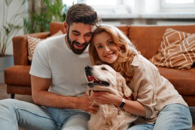 Genç bir çift evdeki oturma odasının penceresinde oturmuş labrador köpeklerine sarılıp oynaşıyor ve birlikte eğleniyorlar..