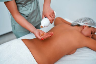 Rahatlamış genç bir kadının masaj masasına yüzüstü uzanması ve profesyonel masör tarafından spa salonunda ya da sağlık merkezinde yapılan vücut masajının keyfini çıkarması.