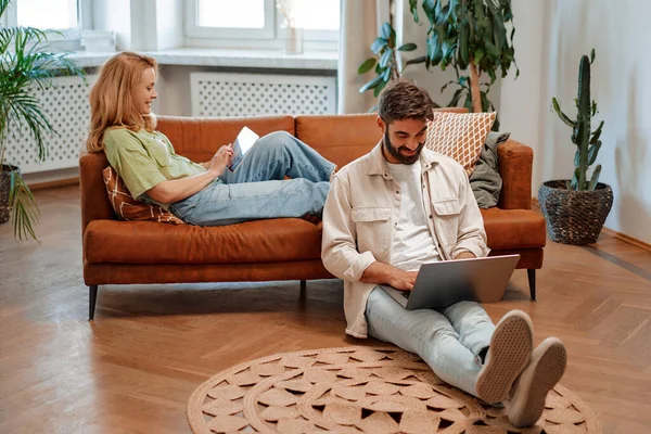 stock image Beautiful adult couple sitting with laptop and tablet in the living room at home, working online, shopping or chatting online.