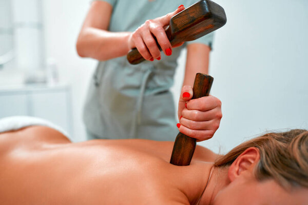 Young woman during a traditional Thai massage tok-sen. Oriental alternative medicine with wooden tools. Body care and SPA in the salon.
