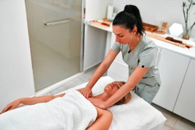 Rahatlamış genç bir kadının masaj masasına uzanması ve masaj salonundaki ya da sağlık merkezindeki profesyonel masörlerin vücut masajının keyfini çıkarması.