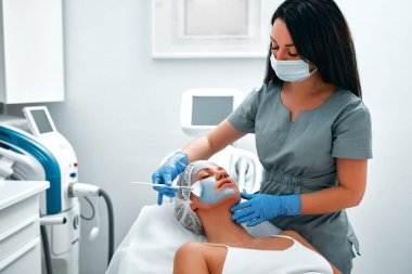 Yüz soyma maskesi, kaplıca güzellik tedavisi, cilt bakımı. Güzellik salonunda güzellik uzmanından yüz bakımı alan bir kadın. Kozmetik uzmanı yüz bakımı yapıyor ve yüz maskesi takıyor