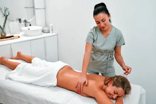 Young relaxed female client lying on medical couch with closed eyes while masseur doing anti stress head massage in the beauty spa salon. Body care and cosmetology concept.