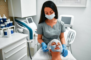 Yüz soyma maskesi, kaplıca güzellik tedavisi, cilt bakımı. Güzellik salonunda güzellik uzmanından yüz bakımı alan bir kadın. Kozmetik uzmanı yüz bakımı yapıyor ve yüz maskesi takıyor