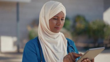 Hastane binasının yakınındaki sokakta steteskoplu ve tesettürlü genç bir Müslüman kadın doktor. İlaç ve sağlık hizmetleri.