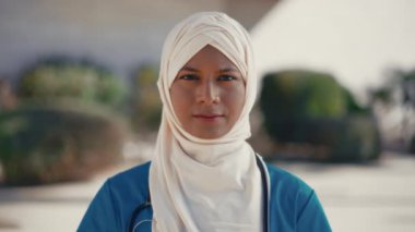 Steteskoplu tesettürlü genç müslüman kadın hastane binasının yanında dururken el hareketini durdurduğunu gösteriyor. İlaç ve sağlık hizmetleri.