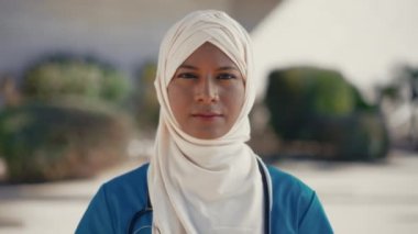 Steteskoplu tesettürlü genç müslüman kadın hastane binasının yakınında ellerini çapraz tutarak dur işareti gösteriyor. İlaç ve sağlık hizmetleri.