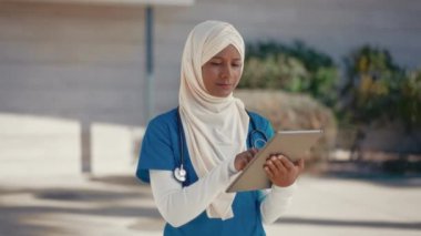 Hastane binasının yakınındaki sokakta steteskoplu ve tesettürlü genç bir Müslüman kadın doktor. İlaç ve sağlık hizmetleri.