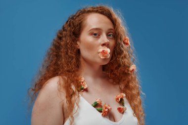 Genç kızıl saçlı, kilolu ya da çiçekli tombul bir kadın doğal bedenini kutluyor. Mavi arka planda beyaz iç çamaşırlı güzel bir kadın model. Kozmetoloji, cilt ve vücut bakımı kavramı.