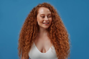 Genç, güzel, kızıl saçlı, kilolu ya da tombul bir kadın doğal bedenini kutluyor. Mavi arka planda beyaz iç çamaşırlı güzel bir kadın model. Vücut pozitifliği, cilt bakımı ve kozmetoloji.