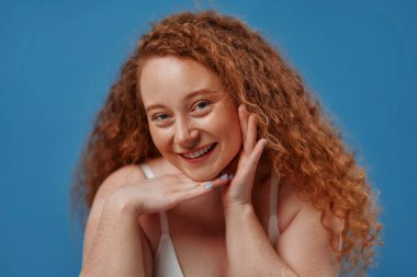 Genç, güzel, kızıl saçlı, kilolu ya da tombul bir kadın doğal bedenini kutluyor. Mavi arka planda beyaz iç çamaşırlı güzel bir kadın model. Vücut pozitifliği, cilt bakımı ve kozmetoloji.