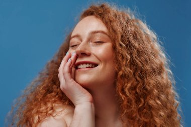 Kızıl saçlı, çilli, şişman, beyaz iç çamaşırlı, şişman, mavi arka planda soyutlanmış bir kadın. Vücut pozitifliği, cilt bakımı ve kozmetoloji.