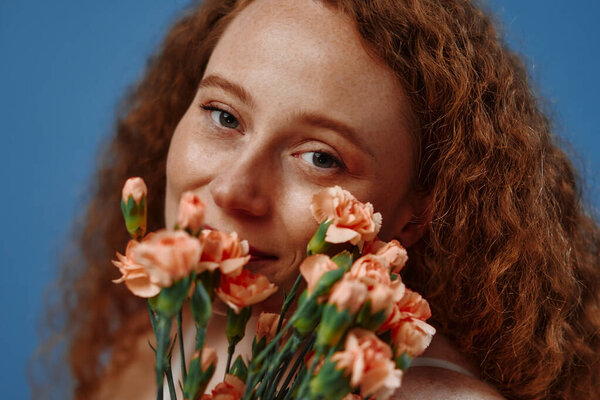 Молодая рыжая плюс размер или пухлая женщина с цветами, празднующих ее естественное тело. Красивая модель в белом нижнем белье на голубом фоне. Косметология, уход за кожей и телом.