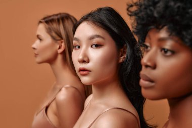 Bej iç çamaşırlı çok ırklı genç kadınlar bej arka planda izole edilmiş. Stüdyoda poz veren Afro-Amerikalı, Kafkas ve Asyalı kadınlar. Yüz bakımı, kozmetoloji kavramı.