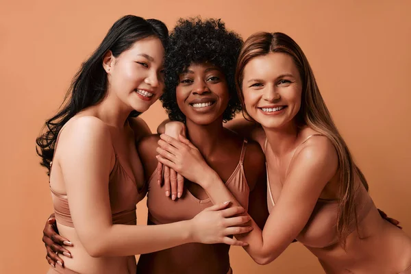 stock image Multi-ethnic multiracial young women in beige lingerie isolated on a beige background. African-American, Caucasian and Asian women posing in the studio. Concept of face body skin care, cosmetology.