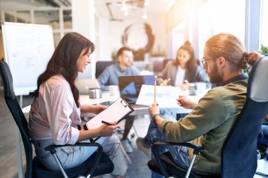 Bir grup genç iş adamı modern ofiste birlikte çalışıyor. Bilgisayarı, tableti, akıllı telefonu, defteri olan yaratıcı insanlar. Birlikte çalışan başarılı bir hipster takımı. Bağımsızlar.