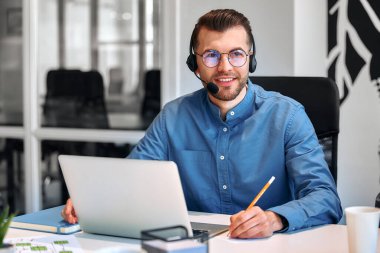 Ekibiyle birlikte çağrı merkezi çalışanı. Erkek işadamı serbest çalışan, birlikte çalışan, modern bir ofis. Kulaklık ve dizüstü bilgisayarla çalışan genç bir çalışan.