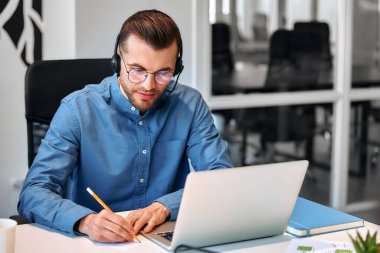 Ekibiyle birlikte çağrı merkezi çalışanı. Erkek işadamı serbest çalışan, birlikte çalışan, modern bir ofis. Kulaklık ve dizüstü bilgisayarla çalışan genç bir çalışan.