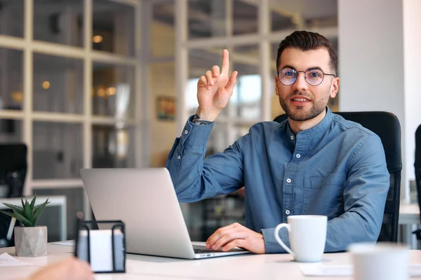 stock image Young bearded handsome businessman in glasses and shirt sitting in a modern office with a laptop with a cup of coffee. Successful hipster team in coworking. Freelancers.