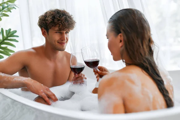 セクシーなロマンチックな若いカップルは赤ワインを飲み 泡風呂に入ります 情熱的な女性ありますリラックスしていますバスルームで彼女の可愛いですボーイフレンド — ストック写真