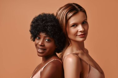 Beyaz ve Afro-Amerikan bir kadının portresi. Bej bir arka planda izole edilmiş parlak bir cildi var. Kozmetik ve kaplıca tedavileri. Cilt bakımı kavramı.