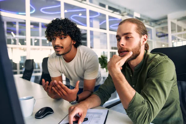 Two multiracial male freelancers discussing work and business in a modern coworking office while sitting at a computer. Colleagues argue, badly done job.
