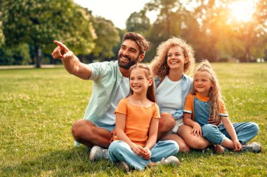 Mutlu, genç bir aile babası, anne ve iki kızı sıcak güneşli bir günde parkta çimlerin üzerinde oturuyor, birlikte eğleniyor ve eğleniyor, izin günlerinde dinleniyorlar..