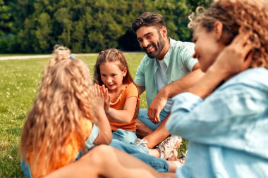 Mutlu, genç bir aile babası, anne ve iki kızı sıcak güneşli bir günde parkta çimlerin üzerinde oturuyor, birlikte eğleniyor ve eğleniyor, izin günlerinde dinleniyorlar..