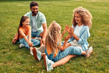 Mutlu, genç bir aile babası, anne ve iki kızı sıcak güneşli bir günde parkta çimlerin üzerinde oturuyor, birlikte eğleniyor ve eğleniyor, izin günlerinde dinleniyorlar..