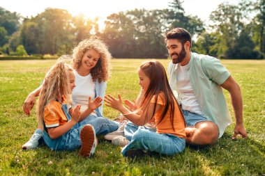 Mutlu, genç bir aile babası, anne ve iki kızı sıcak güneşli bir günde parkta çimlerin üzerinde oturuyor, birlikte eğleniyor ve eğleniyor, izin günlerinde dinleniyorlar..