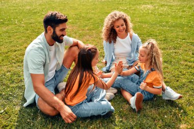 Mutlu, genç bir aile babası, anne ve iki kızı sıcak güneşli bir günde parkta çimlerin üzerinde oturuyor, birlikte eğleniyor ve eğleniyor, izin günlerinde dinleniyorlar..