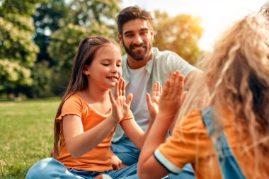 Mutlu, genç bir aile babası, anne ve iki kızı sıcak güneşli bir günde parkta çimlerin üzerinde oturuyor, birlikte eğleniyor ve eğleniyor, izin günlerinde dinleniyorlar..