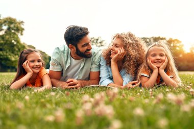 Mutlu, genç bir aile babası, anne ve iki kızı güneşli bir günde parkta çimlerin üzerinde uzanıyor, birlikte eğleniyor ve tatil günlerinde dinleniyorlar..