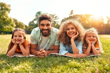 Mutlu, genç bir aile babası, anne ve iki kızı güneşli bir günde parkta çimlerin üzerinde uzanıyor, birlikte eğleniyor ve tatil günlerinde dinleniyorlar..