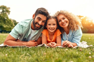 Mutlu, genç bir aile babası, anne ve kızı güneşli bir günde parkta çimlerin üzerinde uzanıyor, birlikte eğleniyor ve tatil günlerinde dinleniyorlar..